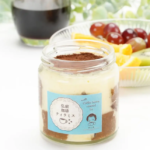Layered dessert in a glass jar with cocoa powder top blue label and fruit platter in the background