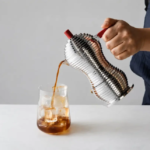 Barista pours coffee from a stainless steel vacuum siphon into a glass with ice