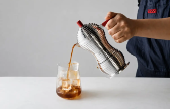 Barista pours coffee from a stainless steel vacuum siphon into a glass with ice