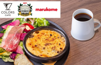 Plate with greens, ham, a baked cheese dish, bread, and a mug of black coffee on a wooden table; top-left white banner shows cafe logos (Colors Cafe, UCC, Marukome).