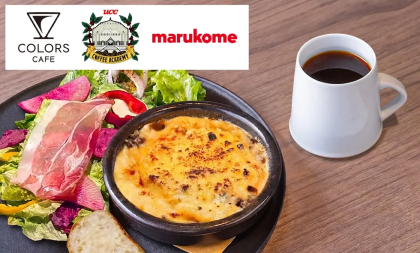 Plate with greens ham a baked cheese dish bread and a mug of black coffee on a wooden table top left white banner shows cafe logos Colors Cafe UCC Marukome