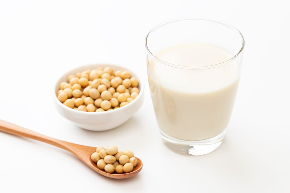 Soybeans in a wooden spoon and a bowl with a glass of soy milk on a white background