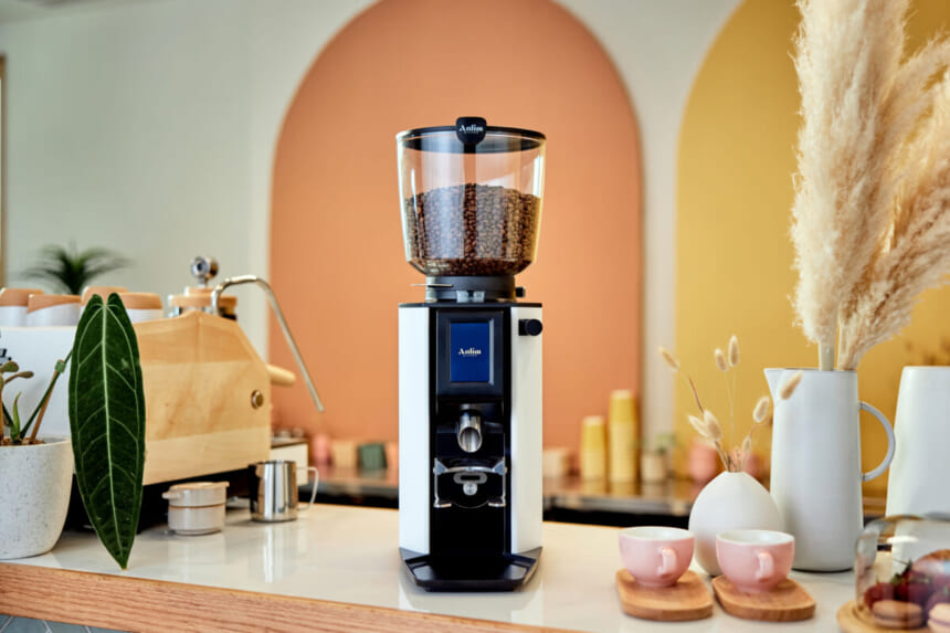 Commercial coffee grinder with glass hopper filled with beans on a white countertop in a bright cafe setting