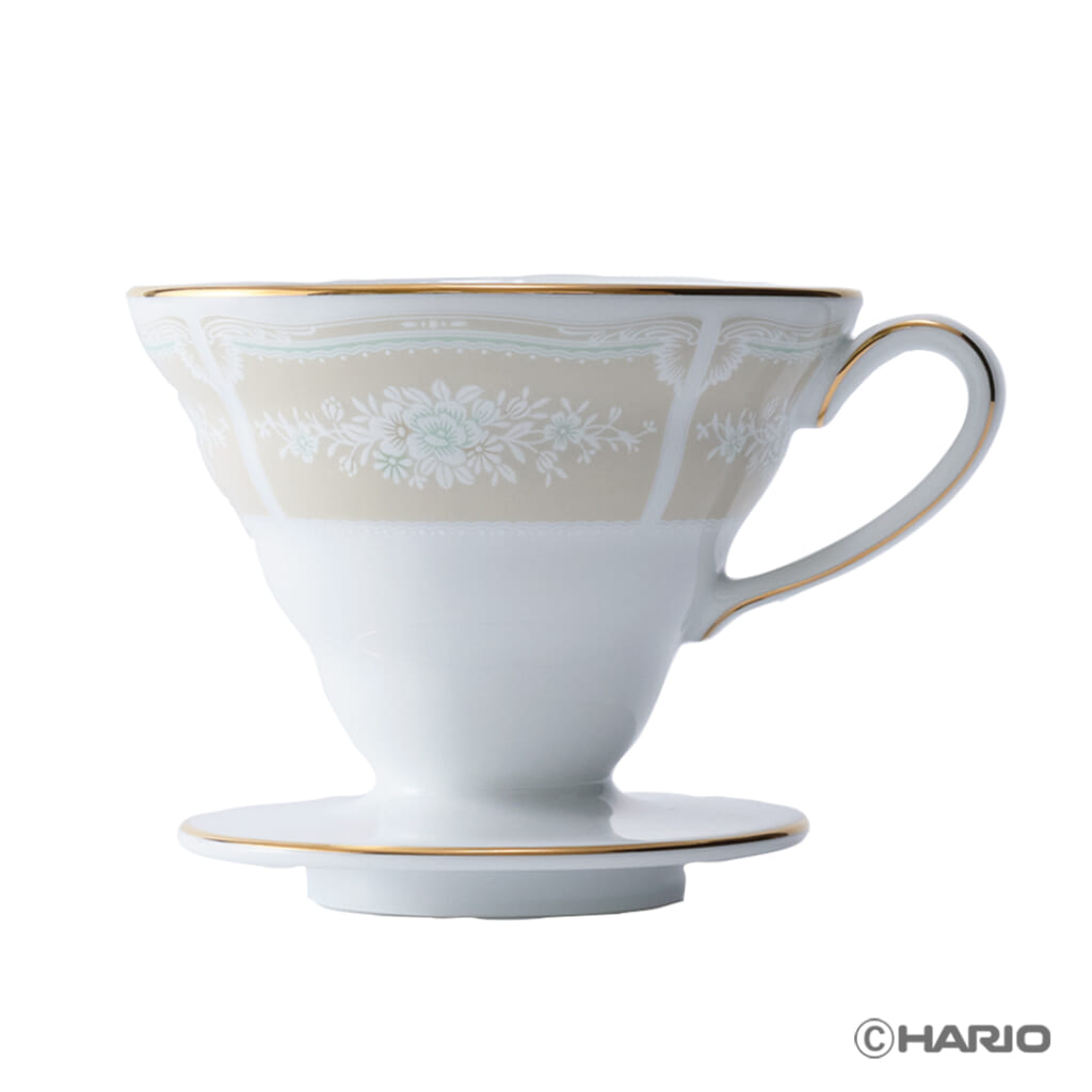 White porcelain teacup with a floral border and gold trim perched on a matching saucer side view