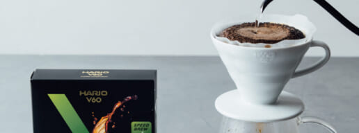 Pour over coffee setup with a white ceramic dripper on a carafe hot water pouring from a black kettle a Hario V60 filter box nearby