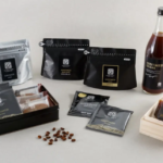 Assorted coffee packaging and a bottle of Geisha coffee with small sample pouches and beans on a light background