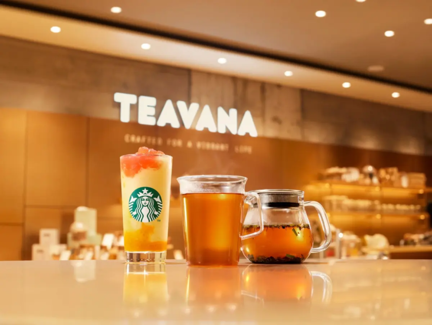 Teavana storefront interior with three beverages on a glossy counter a layered iced drink with Starbucks logo a hot tea and a glass teapot