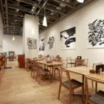 Bright modern cafe interior with wooden tables and chairs pendant lights and large black and white wall art on white walls
