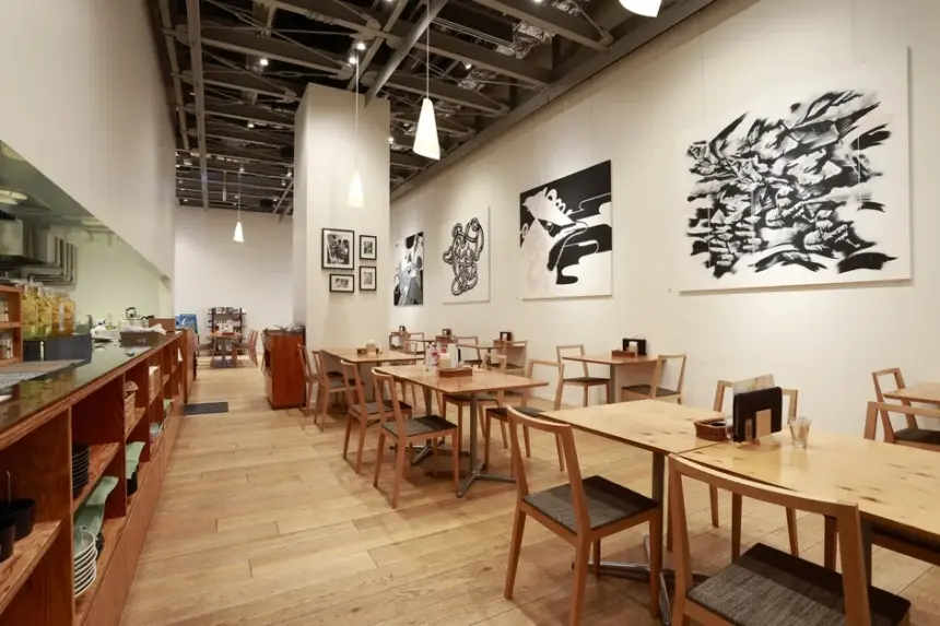 Bright modern cafe interior with wooden tables and chairs pendant lights and large black and white wall art on white walls