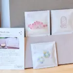 Thank you card and printed materials beside white envelopes with pastel logos on a wooden table small gift boxes in the background