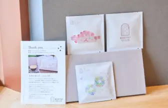Thank you card and printed materials beside white envelopes with pastel logos on a wooden table, small gift boxes in the background.