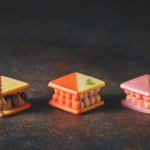 Three triangular mini desserts with layered cream fillings on a dark surface