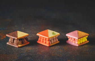 Three triangular mini desserts with layered cream fillings on a dark surface