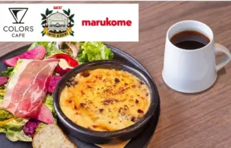 Plate with baked cheese dish, greens, ham slices and bread on a wooden table, with a white coffee mug; logos for Colors Cafe, a coffee academy, and Marukome in the corner.