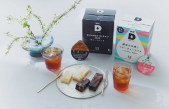Flat lay of UCC drip pod boxes Summer Blend and Seasonal Blend with two iced drinks and a plate of white and dark chocolate bars on a white table surface