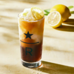 Tall glass of iced beverage with a lime wedge on the rim lemon halves in the background and a star and R logo on the glass