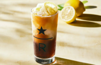 Tall glass of iced beverage with a lime wedge on the rim, lemon halves in the background, and a star and 'R' logo on the glass.