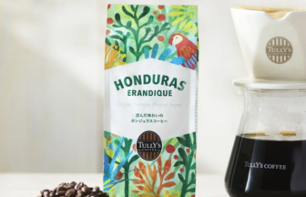 Honduras Erandique coffee bag with vibrant tropical artwork next to a glass coffee carafe and a scoop of roasted beans