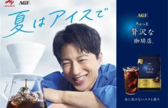 Cheerful man leans on a glass coffee carafe in an iced coffee ad with bold blue Japanese text saying 夏はアイスで and AGF branding on a blue panel to the right