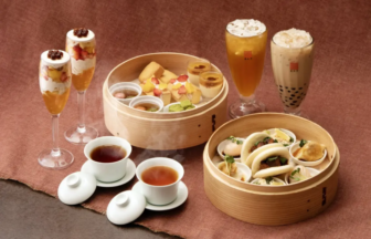 Assorted dim sum in two bamboo steamers with tea and bubble tea on a brown table surface