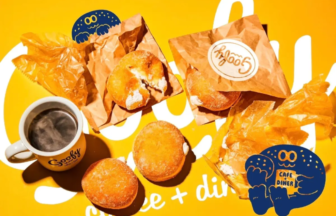 Assorted donuts in brown wrappers scattered on a bright yellow background, with a cup of coffee labeled 'Goofy' and blue cartoon characters nearby.