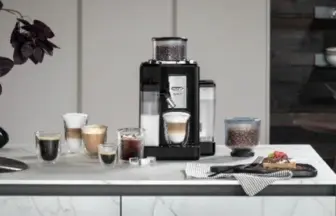 Espresso machine on a kitchen island with several cups of coffee and a pastry plate on the counter.