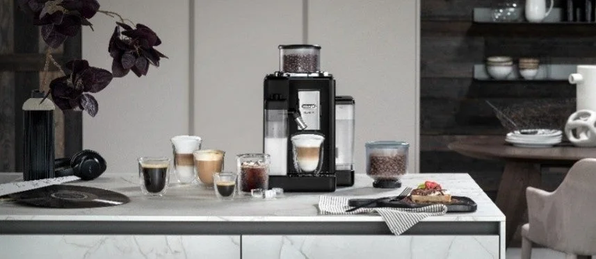 Espresso machine on a kitchen island with several cups of coffee and a pastry plate on the counter
