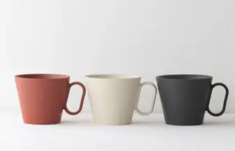Three ceramic mugs in red, cream, and black arranged in a row on a white surface, empty inside.
