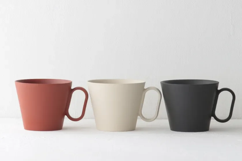 Three ceramic mugs in red cream and black arranged in a row on a white surface empty inside