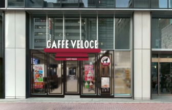 Caffè Veloce cafe storefront with large white signage, red awning, glass doors, and promotional posters in the windows on a city street.