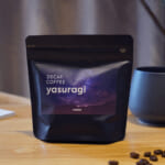 Bag of decaf Yasuragi coffee on a wooden table beside a gray mug with scattered coffee beans nearby