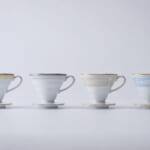 Four delicate teacups with saucers in pastel colors lined up on a white surface green gray beige blue