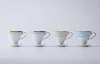 Four delicate teacups with saucers in pastel colors lined up on a white surface green gray beige blue
