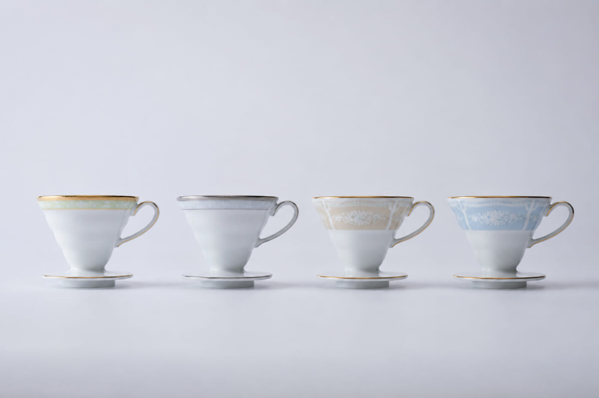 Four delicate teacups with saucers in pastel colors lined up on a white surface green gray beige blue