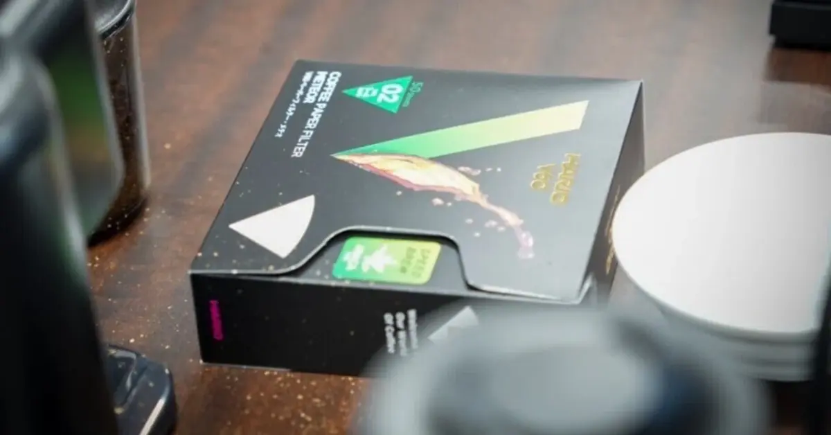 Opened black packaging box with green diagonal graphic on a wooden desk beside a white mug