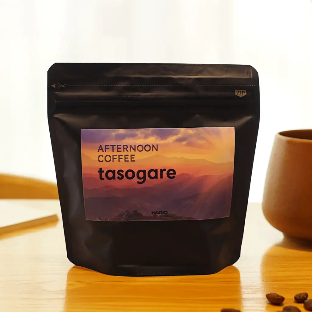 tasogareimagesquare | コーヒーステーション Black resealable coffee bag on a wooden table with a sunset label reading afternoon coffee tasogare and a few coffee beans nearby