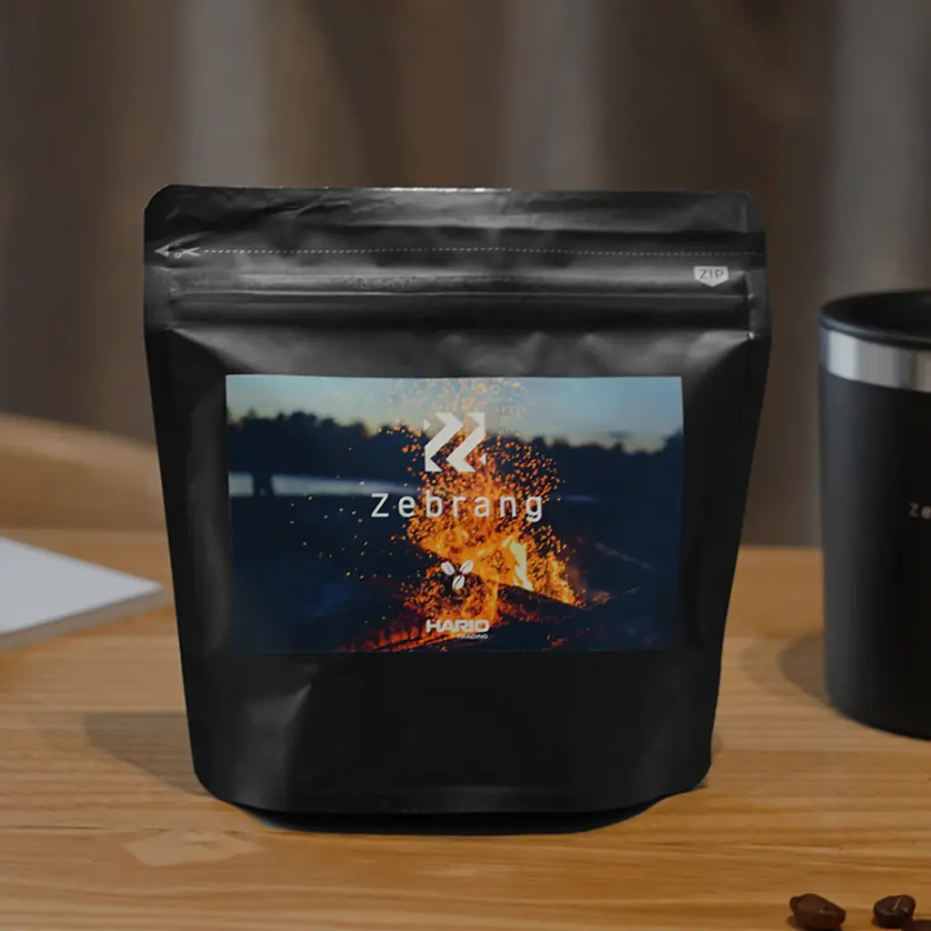 zebrangimagesquareb7334aa9682244d2bf66201e4bd0aefa | コーヒーステーション Black resealable pouch with a photo label showing Zebrang branding and a campfire image on a wooden table