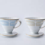 Two fine porcelain teacups with floral bands gold rims and matching saucers on a white background