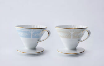 Two fine porcelain teacups with floral bands, gold rims, and matching saucers on a white background.