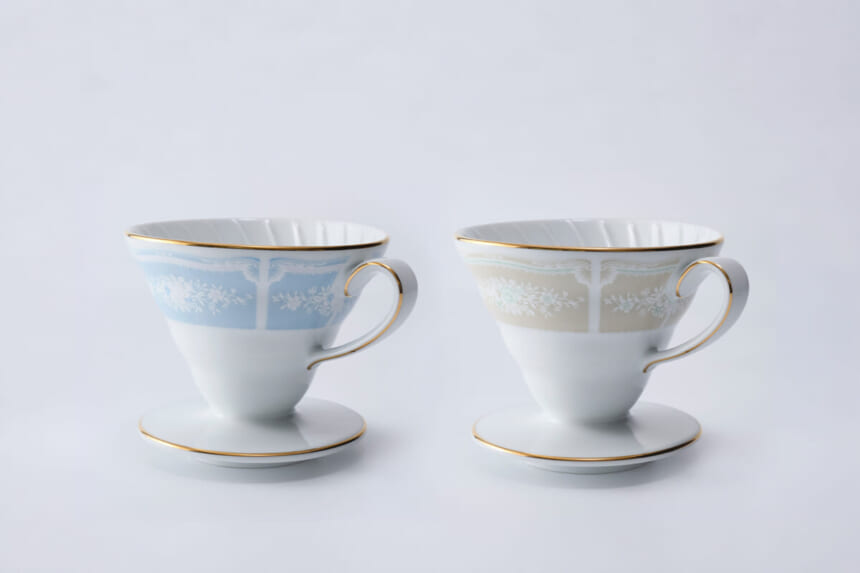 Two fine porcelain teacups with floral bands gold rims and matching saucers on a white background