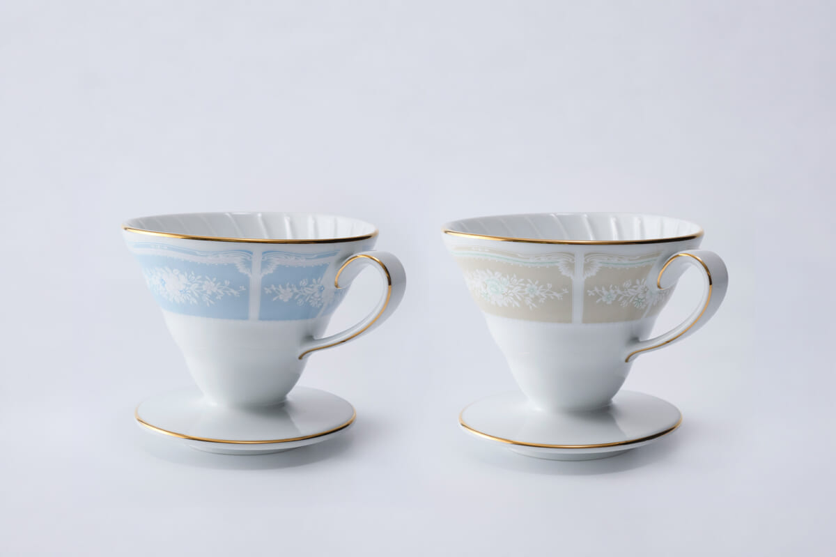 Two fine porcelain teacups with floral bands gold rims and matching saucers on a white background