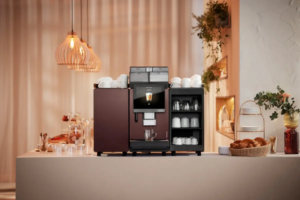 Professional espresso machine on a kitchen counter with cups on top and an open mug rack beside it in warm ambient light