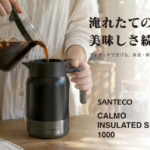 Person pours hot coffee from a glass carafe into a black Santeco Calmo insulated server on a wooden table poster