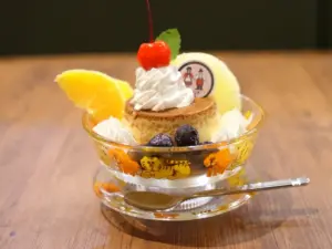 Custard dessert in a patterned glass topped with whipped cream a cherry orange slice blueberries and mint