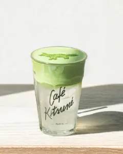 Glass of green matcha latte with frothy top and Café Kitsuné Paris logo on the glass