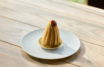 Mont Blanc dessert: chestnut cream strands shaped into a cone on a white plate, topped with a chestnut and herb, on a light wooden table.