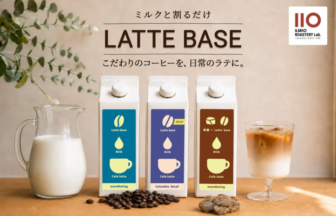 Three Latte Base cartons blue purple brown with milk drops and cups plus a pitcher of milk coffee beans and an iced latte on a wooden table