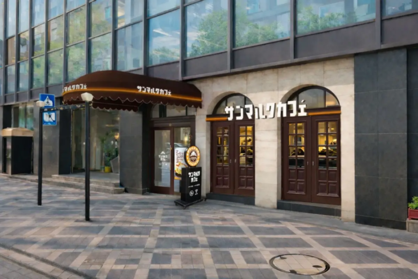 Cafe storefront on a city street with arched windows double wooden doors and a dark stone facade Japanese signage above the entrance and a brown awning