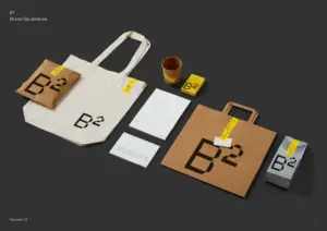 Brand guidelines set displayed on a dark backdrop tote bag paper bag yellow tags calendar sheets business cards and boxes all branded with B² logo