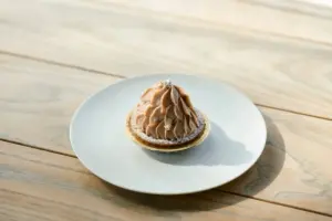 Chocolate mousse pastry with piped rosettes on a thin tart shell served on a white plate over a wooden table